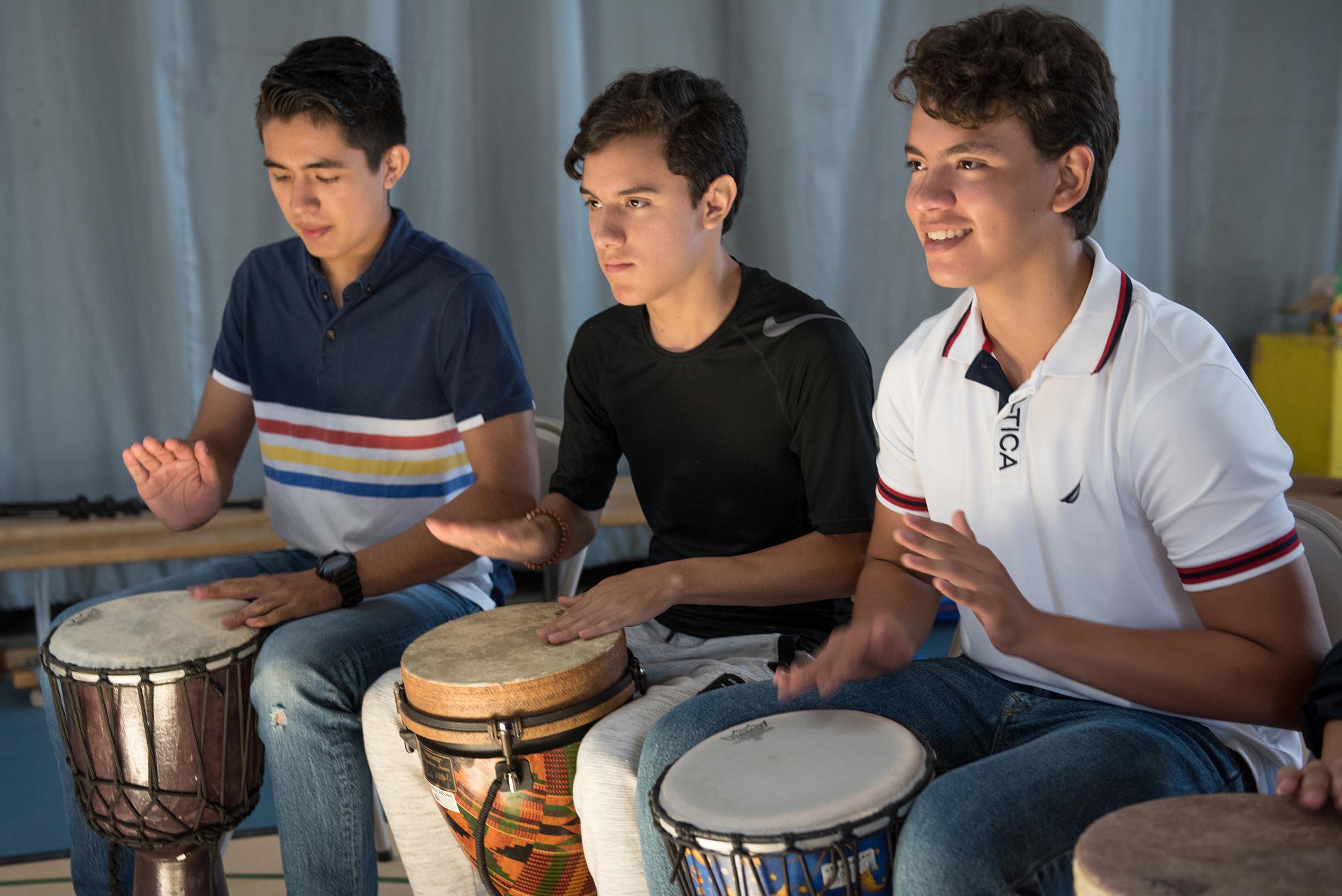 Students sitting next to each other playing the drums Open Gallery
